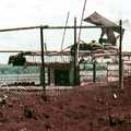 Wooden military structure dug into red soil behind wire mesh fence
