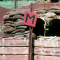 Military structure covered in dirt-filled sacks with a red sign with the letter M in the foreground