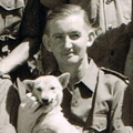 Black and white photograph of men in uniform sitting in rows. One is holding a white dog.