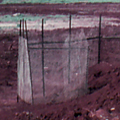 Long line of red soil piled together with military structures behind it and green trees in the background