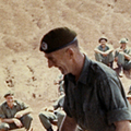 28 October 1969: 1RNZIR RSM Brighouse acts as guest conductor during the band's first performance at the 'Dust Bowl' (Luscombe Bowl), Nui Dat. Military band seated in from of sheets of music watched by groups of men in green military uniforms on hot day