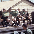 31 October 1969: The band performs for United States wounded at the 93rd EVAC Hospital at Long Binh. Military band playing on wooden stage in front of men wearing blue and green uniforms on hot day