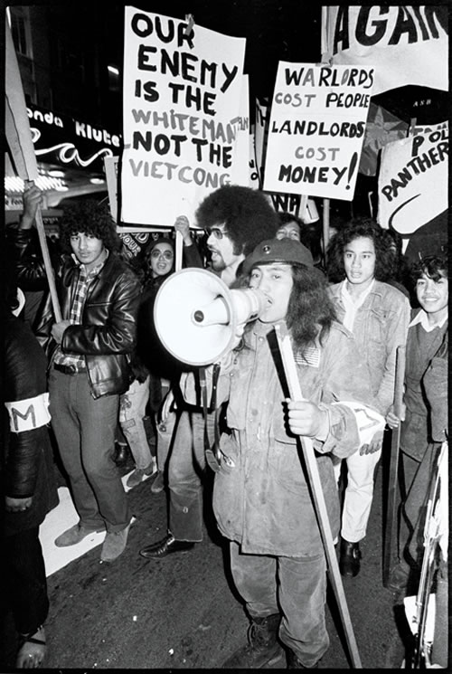 Black and white photograph of Ngā Tamatoa and Polynesian Panthers members marching with signs during an anti-war 'mobilisation' in Auckland, 14 July 1972 