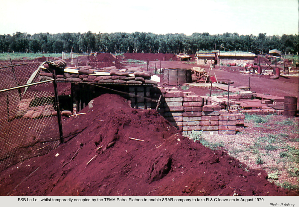 Military structures set amongst red soil with green grass and jungle in the background