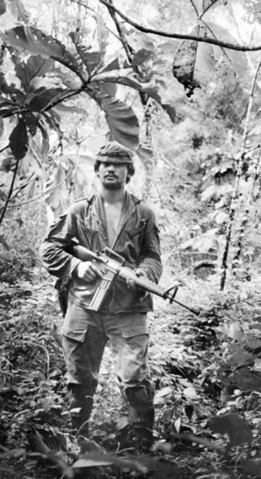 Soldier wearing uniform in jungle holding gun.