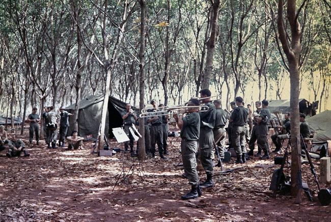 The band plays amongst the rubber trees at FSB Discovery - 1RNZIR Band Tour, 1969