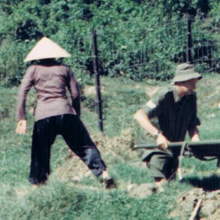 Malcolm Knox Colour photograph of three people in a rough field covered in burnt objects. Two are holding a stretcher.