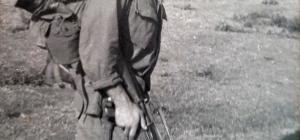 Man in military uniform wearing camouflaged helmet and carrying guns.
