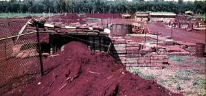 Military structures set amongst red soil with green grass and jungle in the background