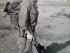 Man in military uniform wearing camouflaged helmet and carrying guns.