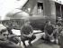 Five men in different military uniforms crouching down in a semi-circle in front of a helicopter