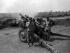 Black and white photograph of two men standing to next to artillery gun as it is fired