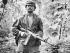 Soldier wearing uniform in jungle holding gun.