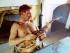 Bare chested man sitting at table holding a guitar.