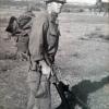 Man in military uniform wearing camouflaged helmet and carrying guns.