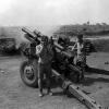 Black and white photograph of two men standing to next to artillery gun as it is fired