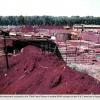 Military structures set amongst red soil with green grass and jungle in the background