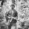 Soldier wearing uniform in jungle holding gun.