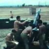 Four shirtless men in green military trousers grouped around a artillery gun