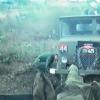 Man in green uniform crouching down next to green coloured truck