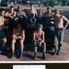 Group of men in khaki military uniform standing and kneeling around artillery gun.