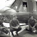 Five men in different military uniforms crouching down in a semi-circle in front of a helicopter