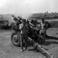 Black and white photograph of two men standing to next to artillery gun as it is fired