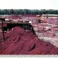 Military structures set amongst red soil with green grass and jungle in the background