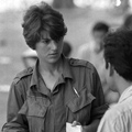 European woman in military style shirt holding notebook and pen looking intensely at Asian man