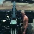 Shirtless man standing next to artillery gun